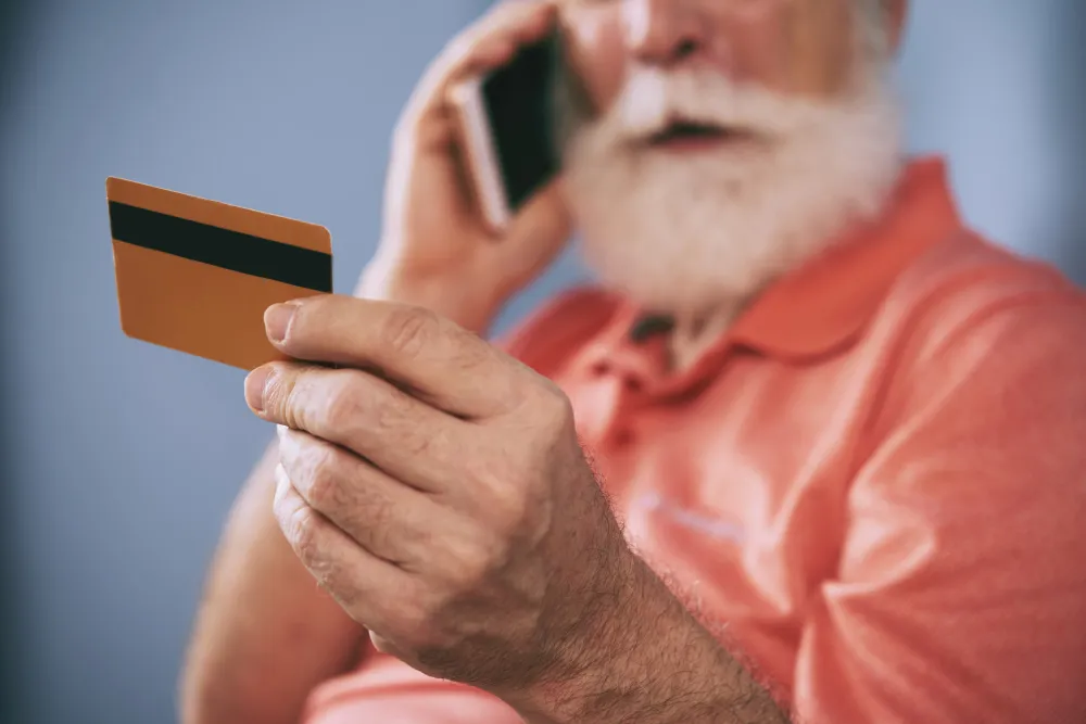 homem idoso falando no celular enquanto segura o cartão - cartão de crédito consignado