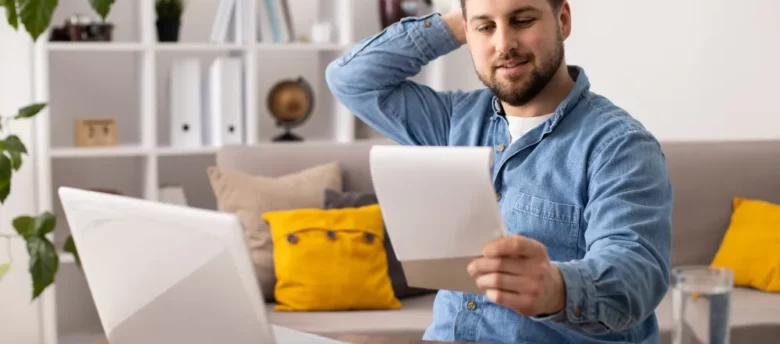 homem sentado em frente ao computador enquanto olha anotações - multa por quebra de contrato de empréstimo