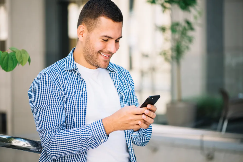 homem sorridente mexendo no celular em casa - tabela pis 2024