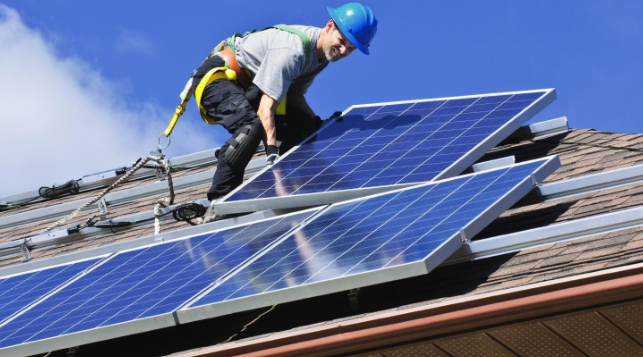 técnico trajado de EPI fazendo manutenção de painel solar em cima de um telhado