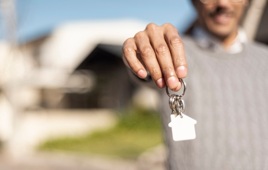 homem segurando chaves de uma casa em primeiro plano com casas ao fundo