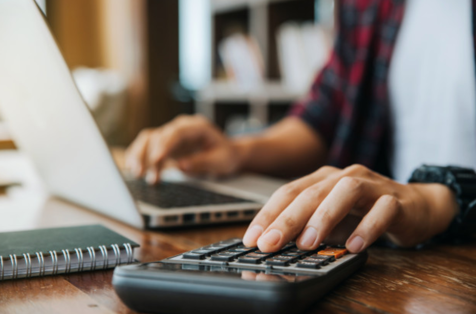 imagem ampliada de homem de camisa xafrez usando um computador e fazendo contas em uma calculadora