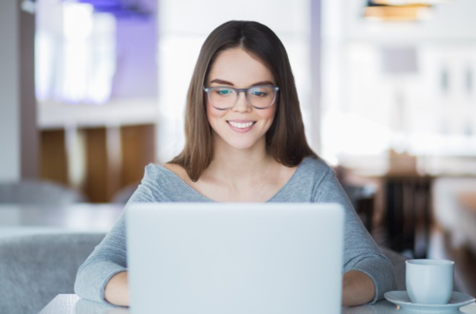 imagem de uma menina de óculos e blusa cinza em frente a um laptop