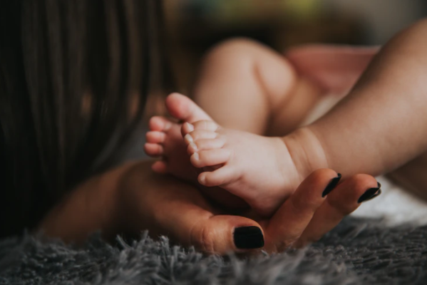 mão de mulher com unhas pretas segurando pés de bebê 