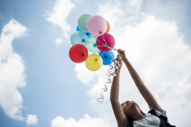 Uma garota segurando balões em direção ao céu