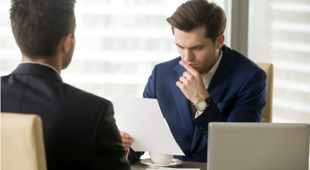 dois homens de terno dentro de um escritório analisando uma folha com medo de investir