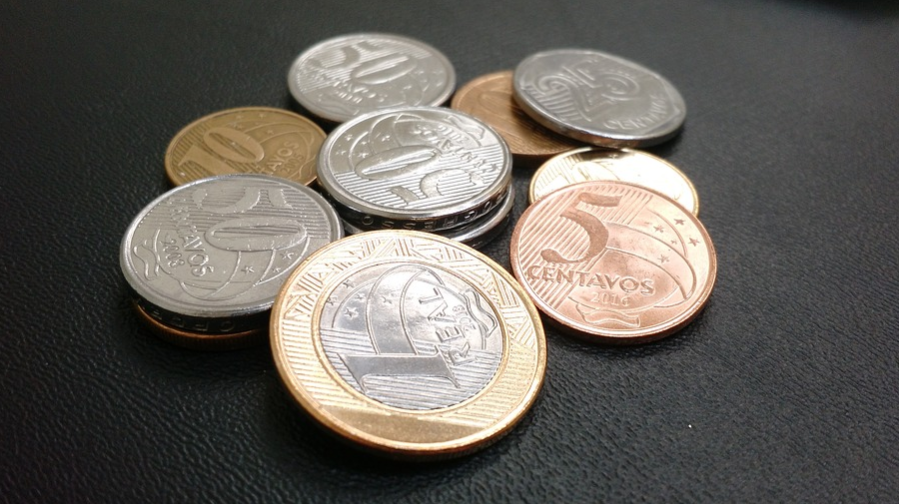 imagem em fundo preto com moedas brasileiras em destaque. Hum real, 5 centavos e 50 centavos estão em evidência. 