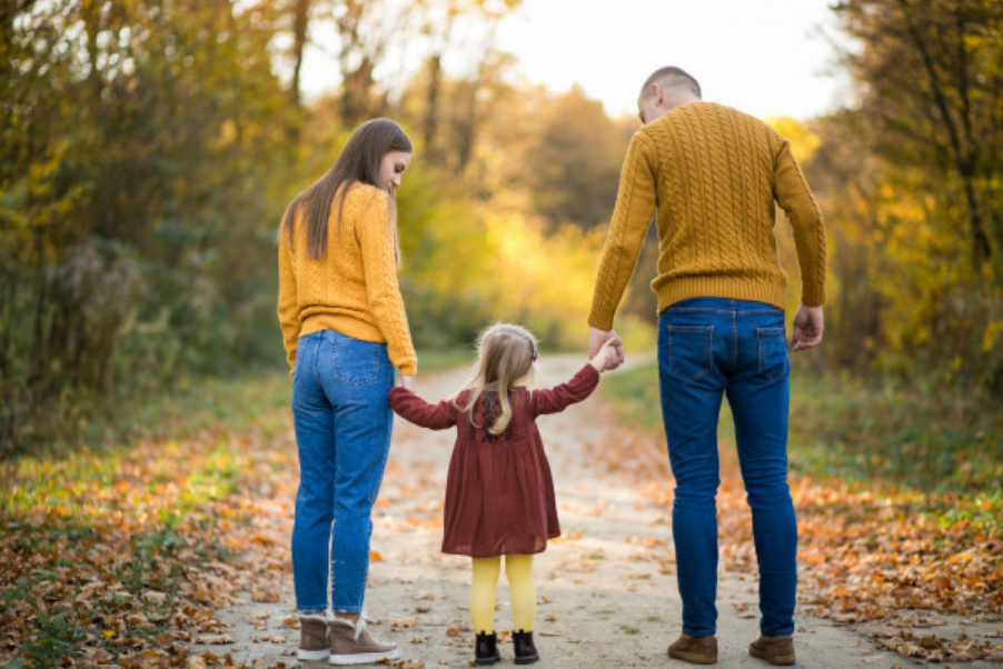 imagem de costas de uma famíliaa formada por pai, mãe e filha, andando por uma estrada