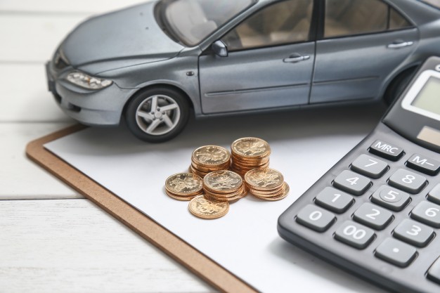 Miniatura de carro em uma mesa com moedas e uma calculadora