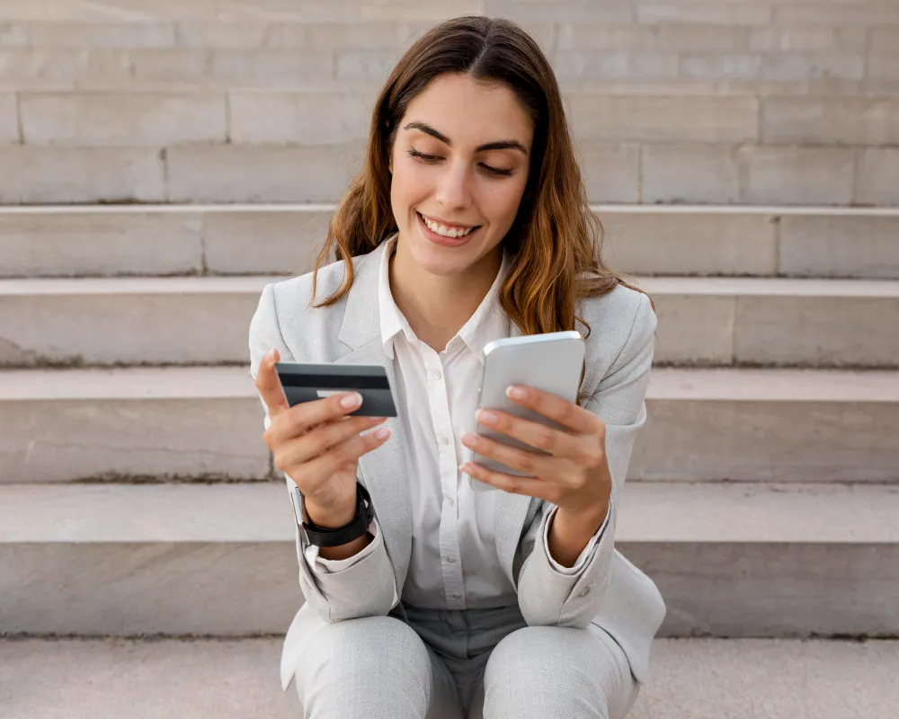 mulher com smartphone-e-cartao-de-credito-enquanto-esta-sentada-na-escada-empréstimo pessoal com garantia de celular