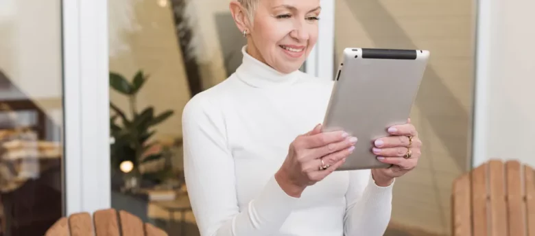 mulher de maior idade com cabelo curto, utilizando tablet em pé - como transferir aposentadoria para outro banco