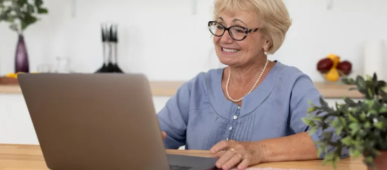 mulher de terceira idade feliz usando computador em casa - empréstimo para aposentado simulação