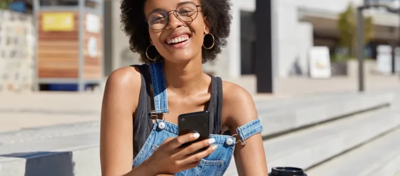 mulher negra ao ar livre sorrindo com café e celular na mão - empréstimo de 300 reais na hora via pix