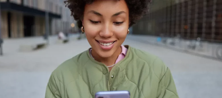 mulher negra mexendo no celular pelas ruas da cidade - empréstimo na conta de luz pelo whatsapp