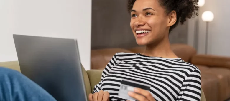 mulher negra sorridente e feliz deitada mexendo no computador com cartão na mão - empréstimo de 1500 reais para negativado