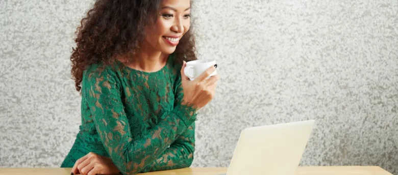 mulher negra tomando café sentada em frente ao computador - qual banco libera cartão de crédito para negativado