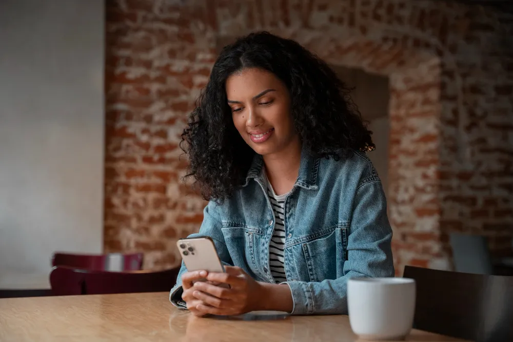 mulher sentada na mesa mexendo no celular com café ao lado - negativação indevida