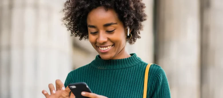 mulher sorridente andando na rua e mexendo no celular - calendário bolsa família 2024