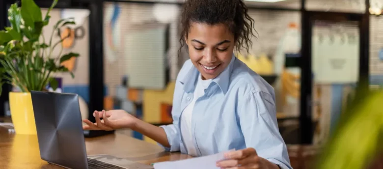 mulher-sorridente-trabalhando-no-escritorio-com-papeis-e-laptop-o que acontece se não declarar Imposto de Renda