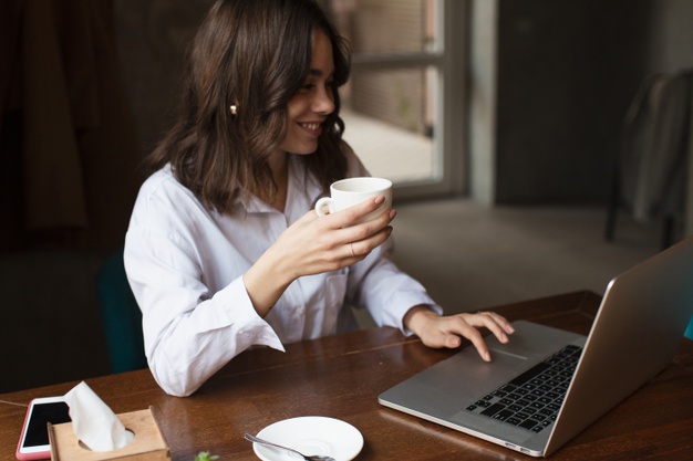 mulher investidora sentada a uma mesa mexendo em seu computador e segurando uma xícara