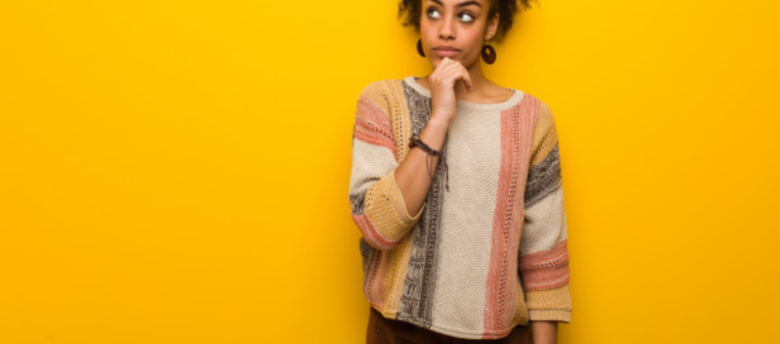 mulher de suéter pensando em frente a uma parede amarela