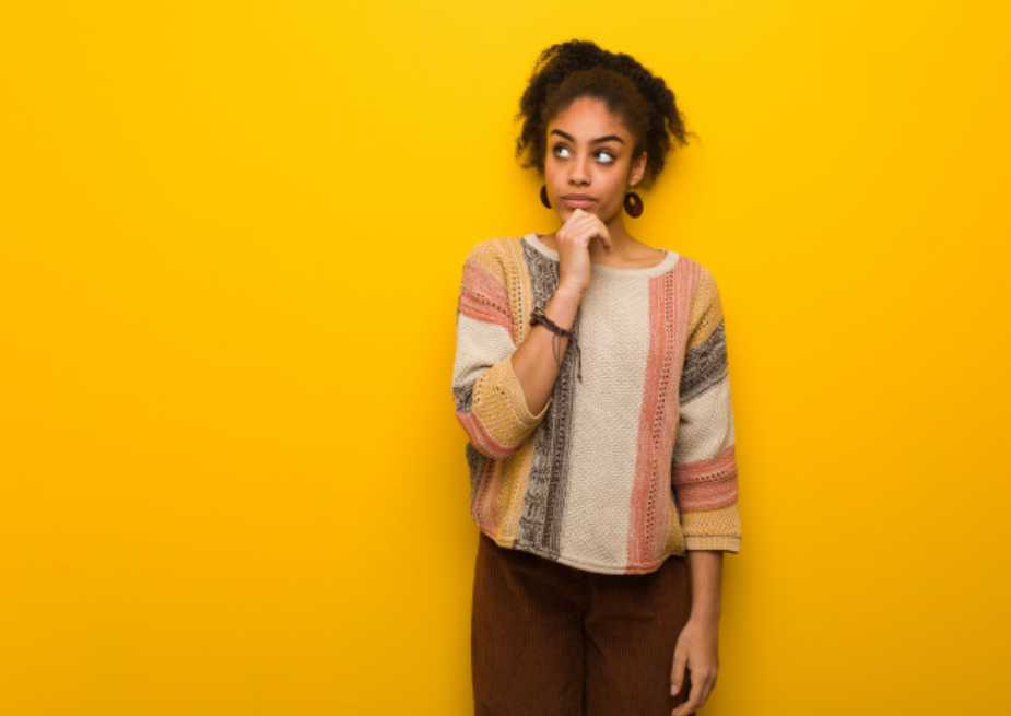 mulher de suéter pensando em frente a uma parede amarela