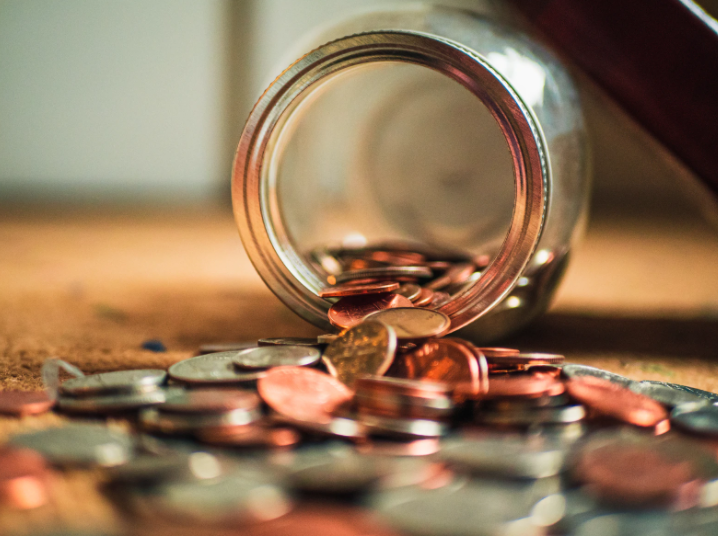 pote de moedas caído em uma mesa com moedas espalhadas pela superfície