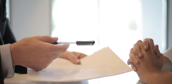 imagem ampliada de duas pessoas sentadas à mesa segurando um papel e uma caneta