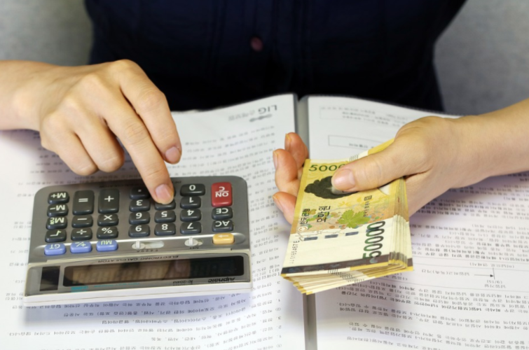 Pessoa com um bolo de dinheiro em uma das mãos e usando calculadora sobre um livro de finanças.