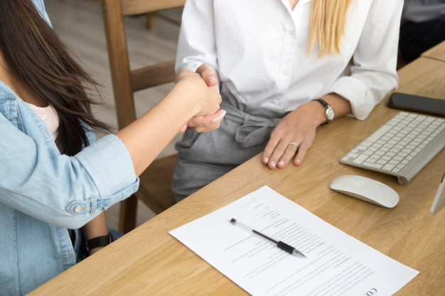 imagem de duas mulheres sentadas a uma mesa apertando as mãos após assinar um contrato
