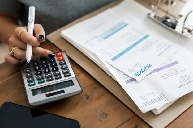 mulher com calculadora, caneta e várias contas sobre uma mesa