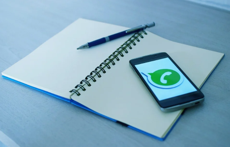 mesa com caderno, caneta e celular com o símbolo do whatsapp na tela