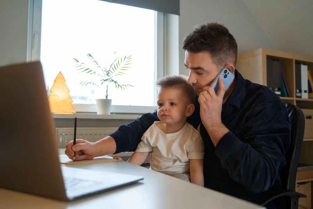 pai com filho no colo em frente ao computador enquanto fala no celular - empréstimo bolsa família quando vai ser liberado