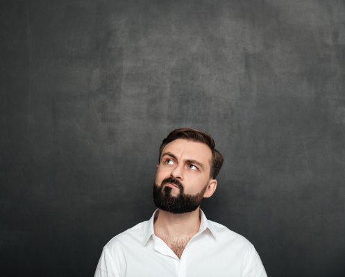 homem de camisa branca usando barba de pé à frente de fundo cor grafite pensando sobre como solicitar o interveniente auitante