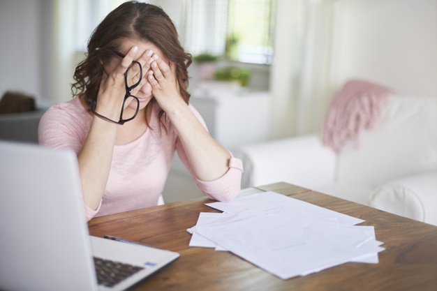 mulher na frente do computador preocupada com as dívidas colocando as mãos no rosto