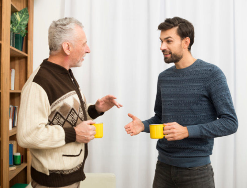 imagem de um homem jovem conversando com um senhor de idade enquanto ambos tomam um café