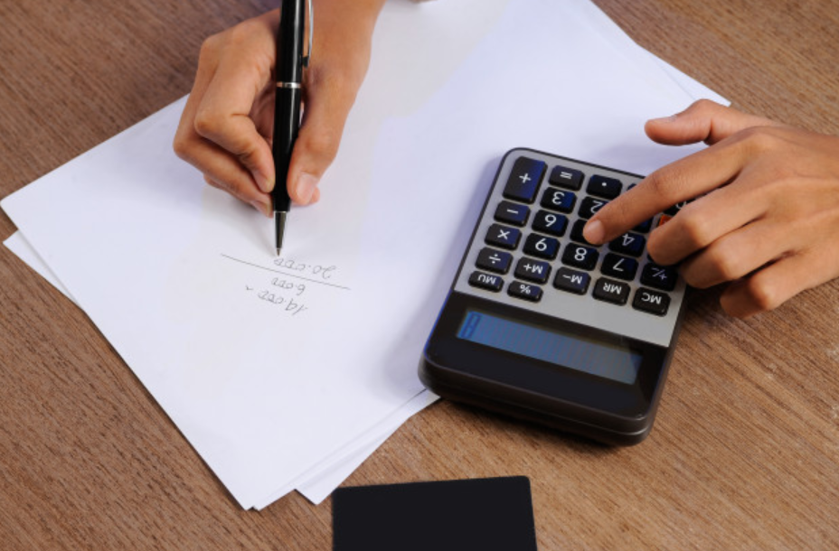 imagem ampliada de uma pessoa usando uma calculadora para fazer contas em um papel sulfite branco