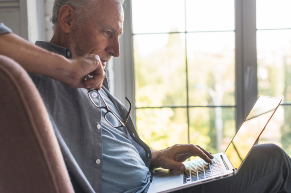 senhor de idade sentado em uma poltrona usando um laptop
