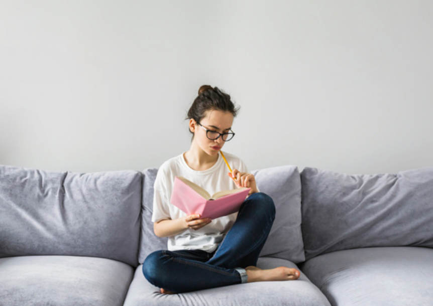 mulher de óculos sentada em sofá cinza fazendo anotações em um caderno