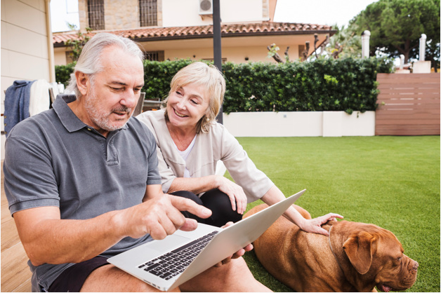 casal de homem e mulher sentados em área externa usando um laptop e acariciando um cachorro