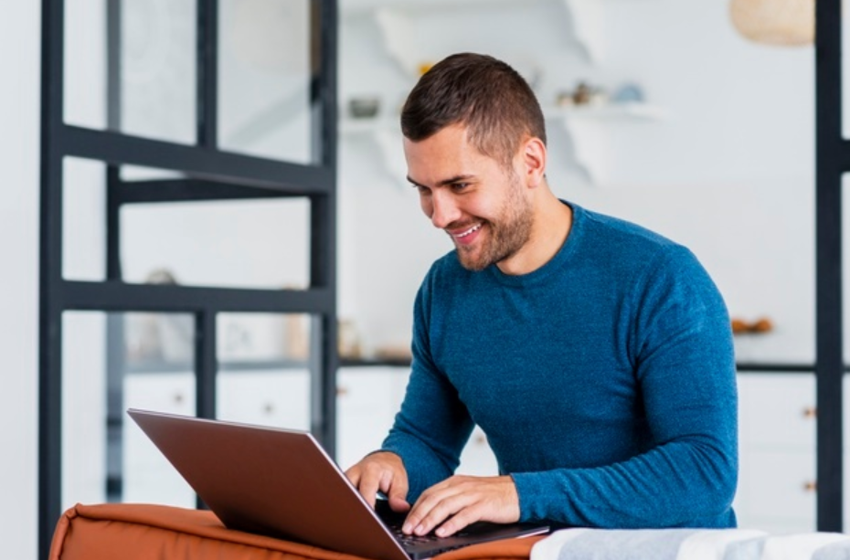 homem de camiseta azul sorrindo e usando seu laptop