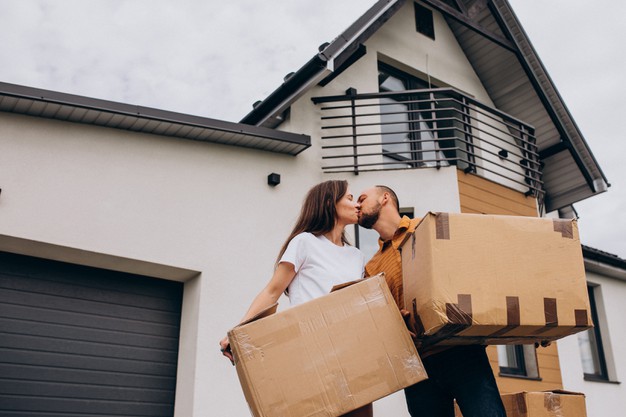 casal se beija segurando caixas em frente a sua casa