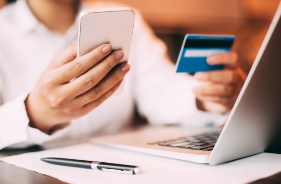 imagem ampliada de uma mulher segurando um cartão de crédito e uma celular em frente a um laptopde crédito e 