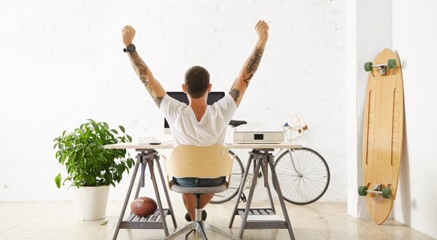 homem de costas sentado a uma mesa de trabalho ao lado de uma prancha e em frente a uma bicicleta