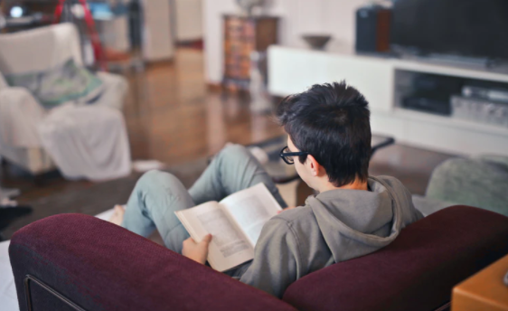 Homem em casa sentado em uma poltrona lendo um livro