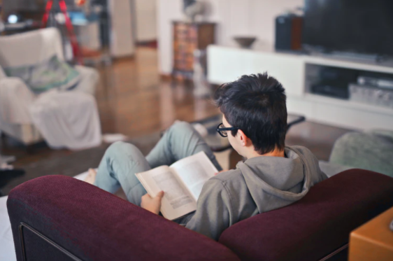 Homem em casa sentado em uma poltrona lendo um livro