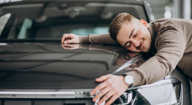 homem de blazer marrom e relógio sorri enquanto abraça um carro