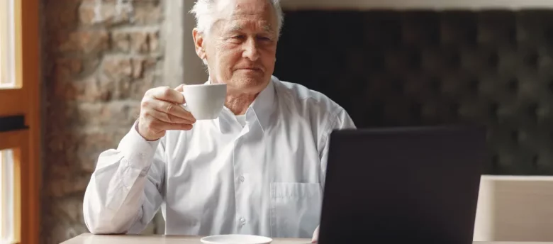 senhor de idade segurando café em frente ao computador - empréstimo pessoal para aposentado negativado