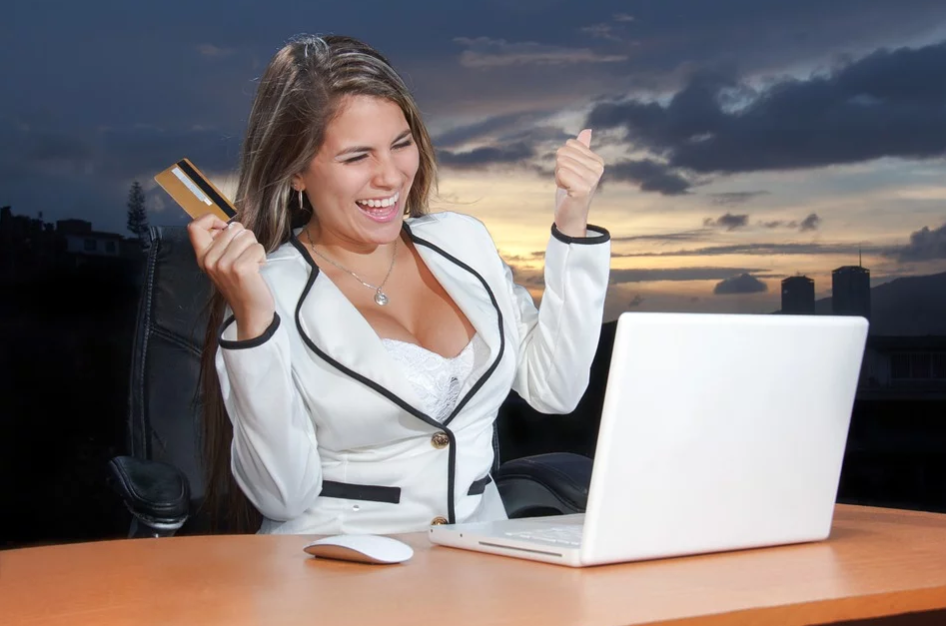 imagem de mulher sorrindo na frente do seu notebook com o cartão de crédito nas mãos