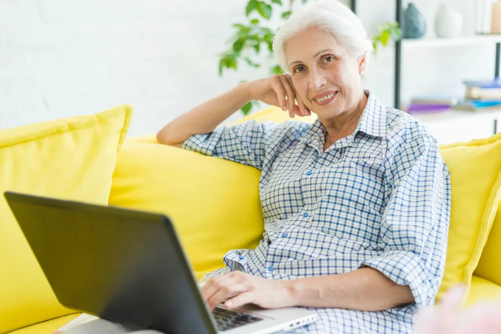 sorrindo-mulher-idosa-sentada-no-sofa-com-laptop-empréstimo consignado para aposentado